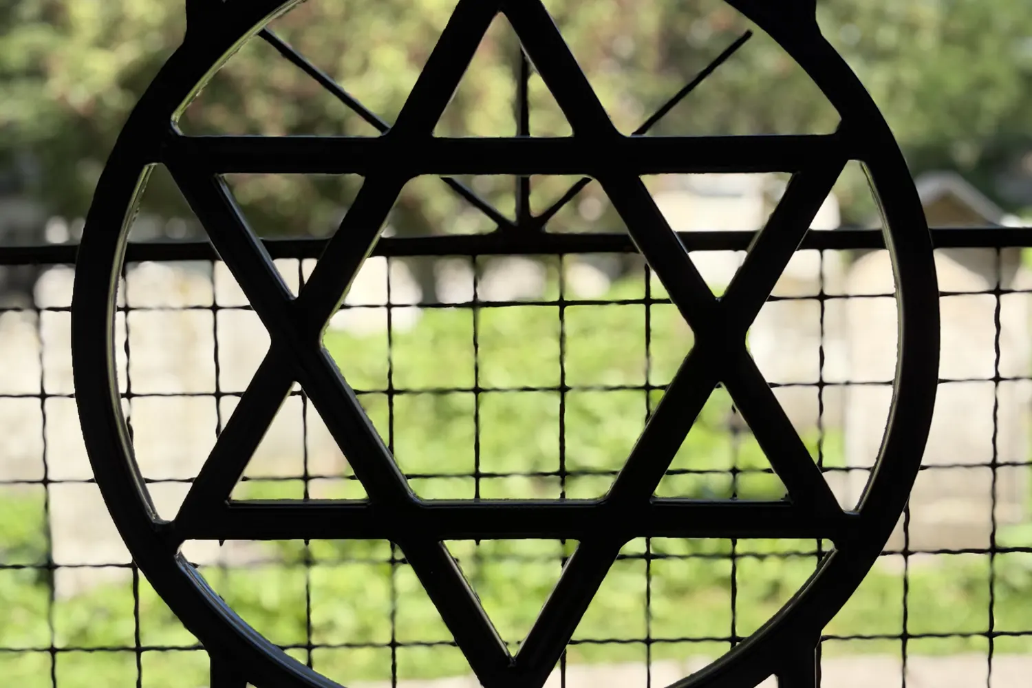 A window in the Remah Cemetery wall with a Star of David grille and a view of the cemetery