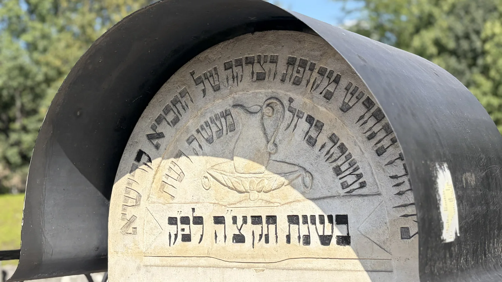 Jewish gravestone with a Hebrew inscription and a relief of a Levite ewer above an oil lamp, under a metal canopy, in a Jewish cemetery in Poland